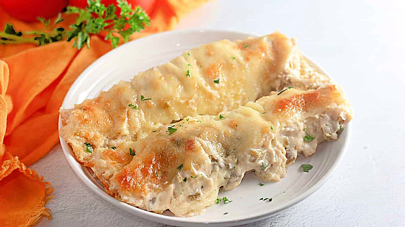 Two White Chicken Enchiladas filled with creamy sauce and topped with melted cheese, served on a white plate with a garnish of chopped parsley.