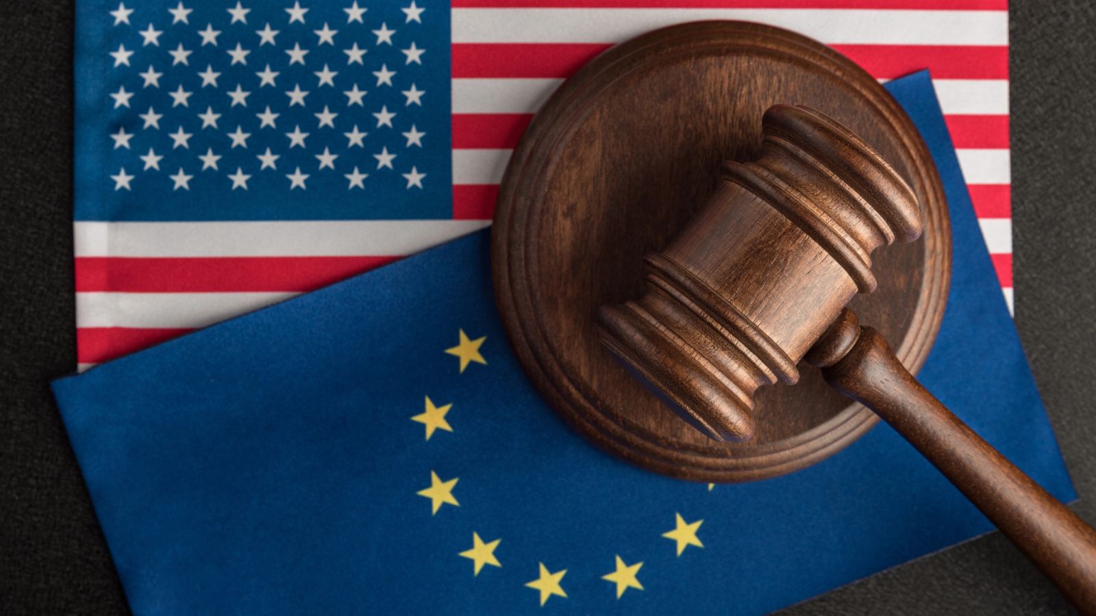 A judge’s gavel rests on overlapping American and European Union flags, symbolizing law or legal matters involving the US and EU, as Americans eat stricter EU rules in cross-border regulations.