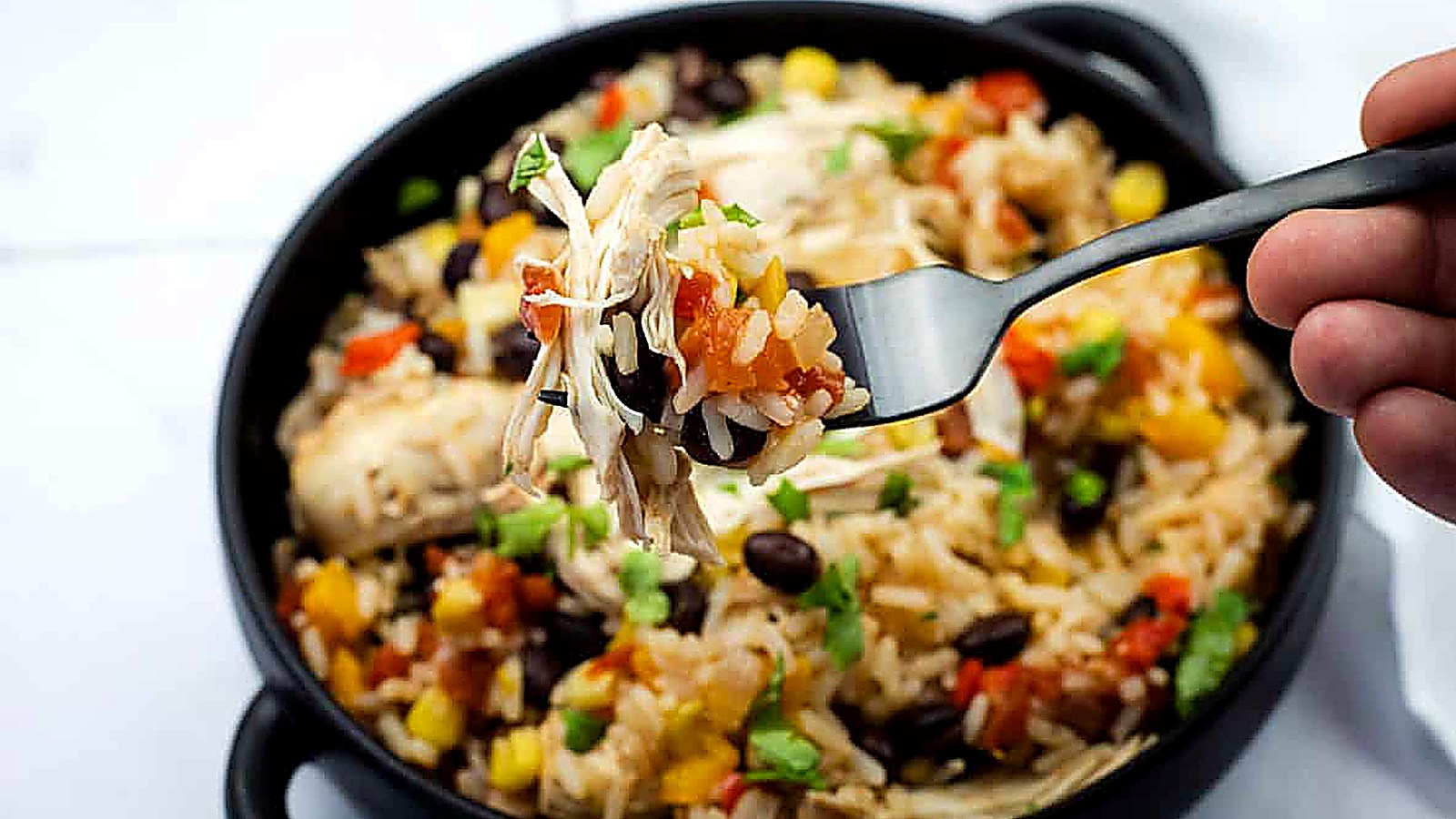 A close-up of a fork holding a bite of Slow Cooker Santa Fe Chicken over a bowl with the same mixed dish.