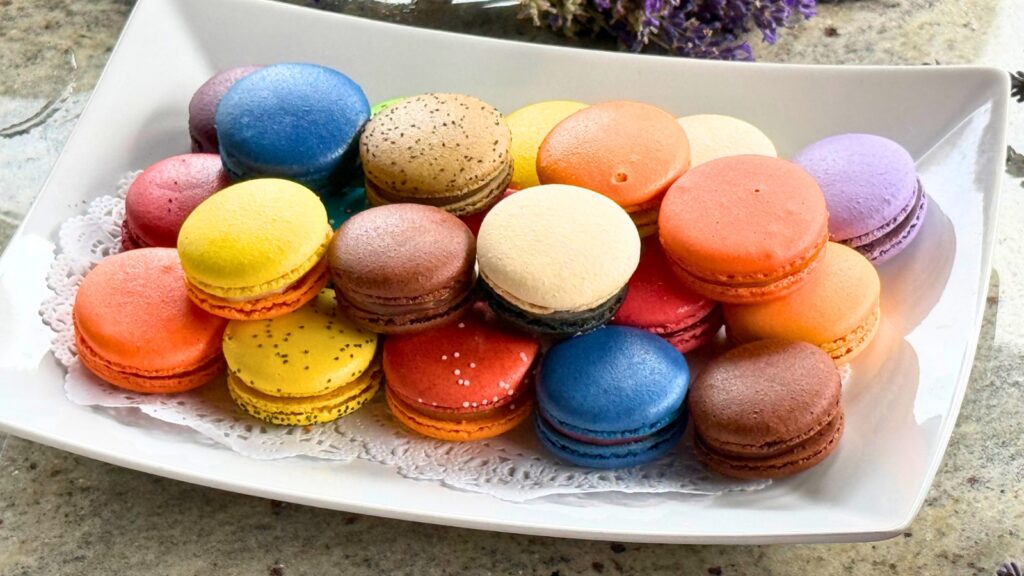 A rectangular white plate holds an assortment of colorful macarons in various flavors, arranged closely together on a lace doily—perfect for savoring a sweet taste of Door County.