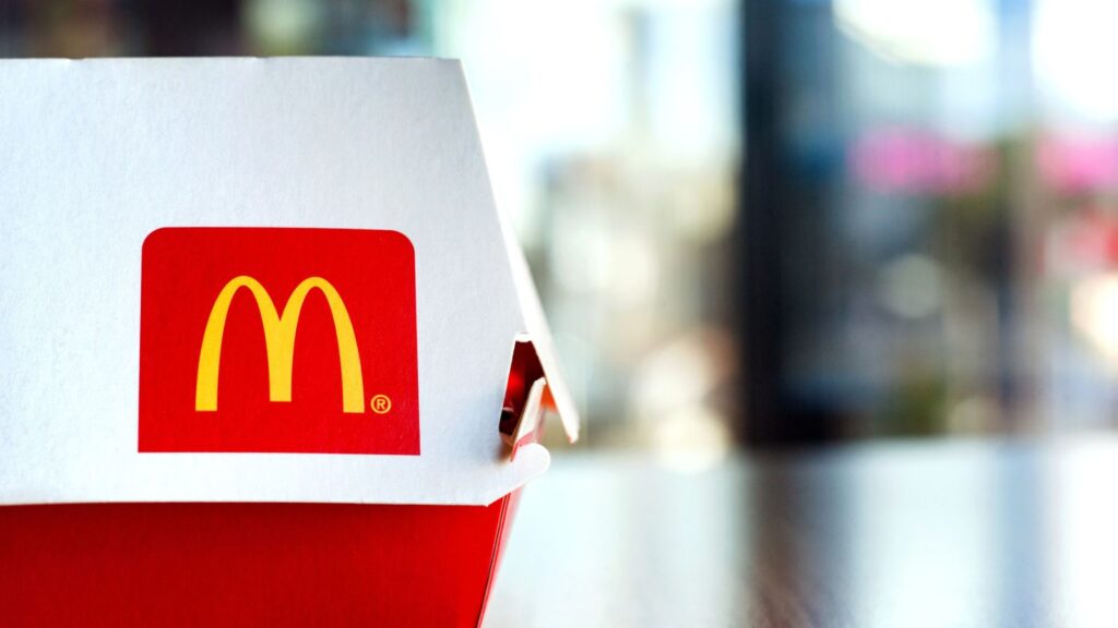 A closed McDonald’s burger box with the yellow “M” logo sits on a table, with a blurred background.