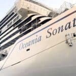 Large white cruise ship named “Oceania Sonata” docked at port, viewed from a low angle. The ship’s name is visible on the hull, with multiple balconies and exterior scaffolding.