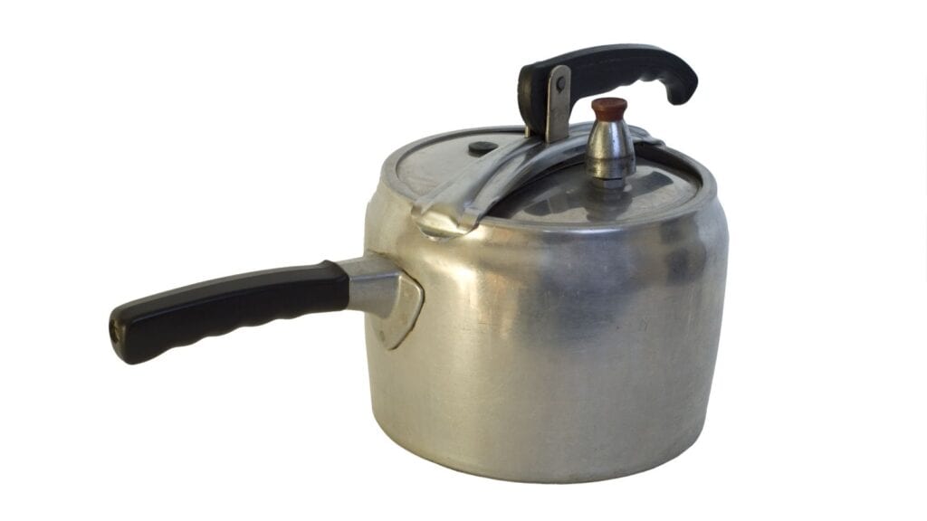 A metal pressure cooker with a black handle and locking lid is shown against a white background, reminiscent of the classic kitchen gear Americans remember from family kitchens.