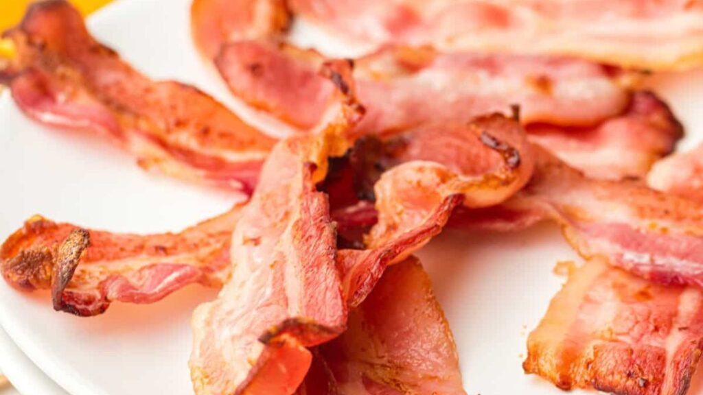 Several strips of cooked bacon are arranged on a white plate.