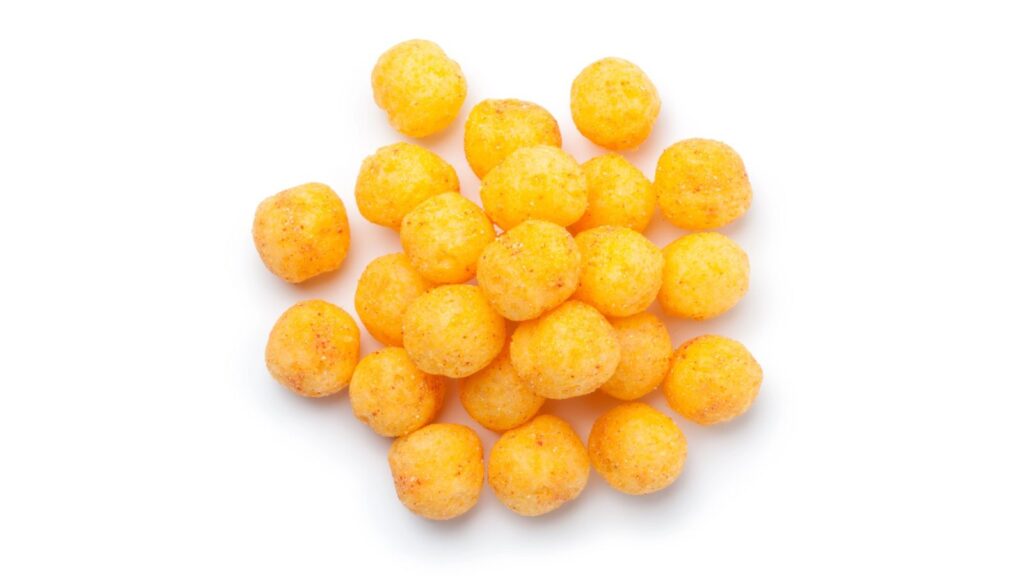 A pile of round, orange cheese-flavored snack puffs on a white background evokes nostalgia for those candy snacks you can’t buy anymore.