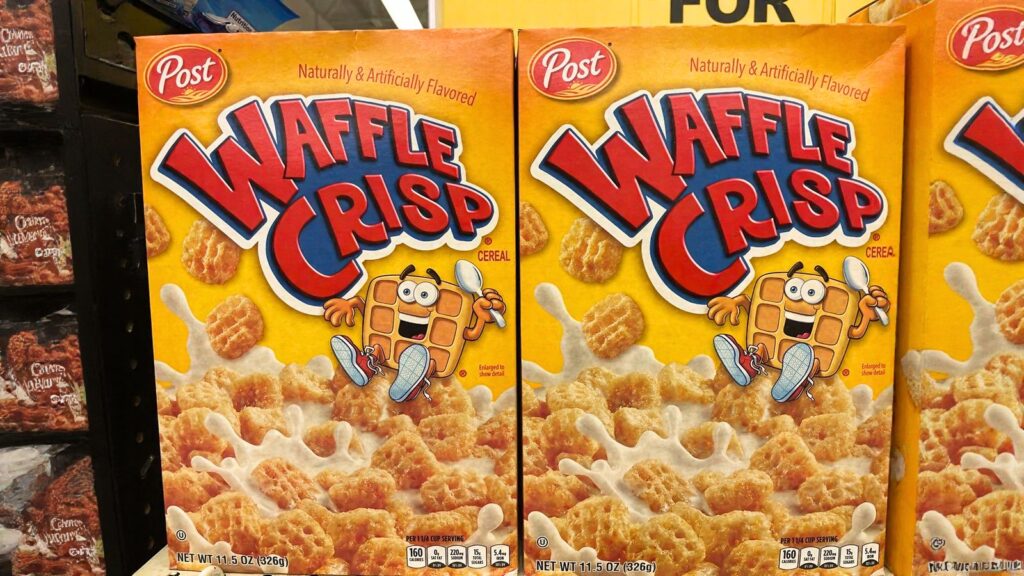 Two boxes of Post Waffle Crisp cereal with cartoon waffle mascot, displayed on a store shelf.