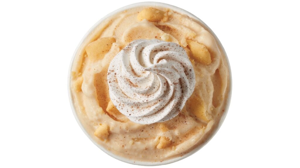 Top view of a creamy Pumpkin Pie Blizzard dessert with a swirl of whipped topping and a sprinkle of cinnamon on an orange-yellow base, served in a round white bowl.
