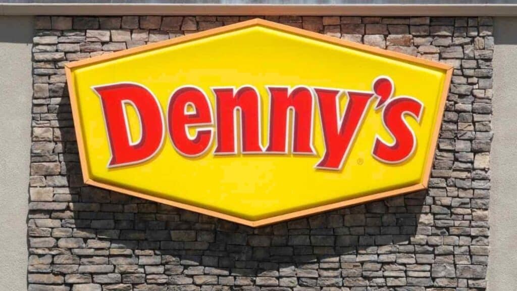 Yellow Denny&rsquo;s restaurant sign with red lettering mounted on a stone wall exterior&mdash;proof that classic diner chains really do seem to be everywhere.