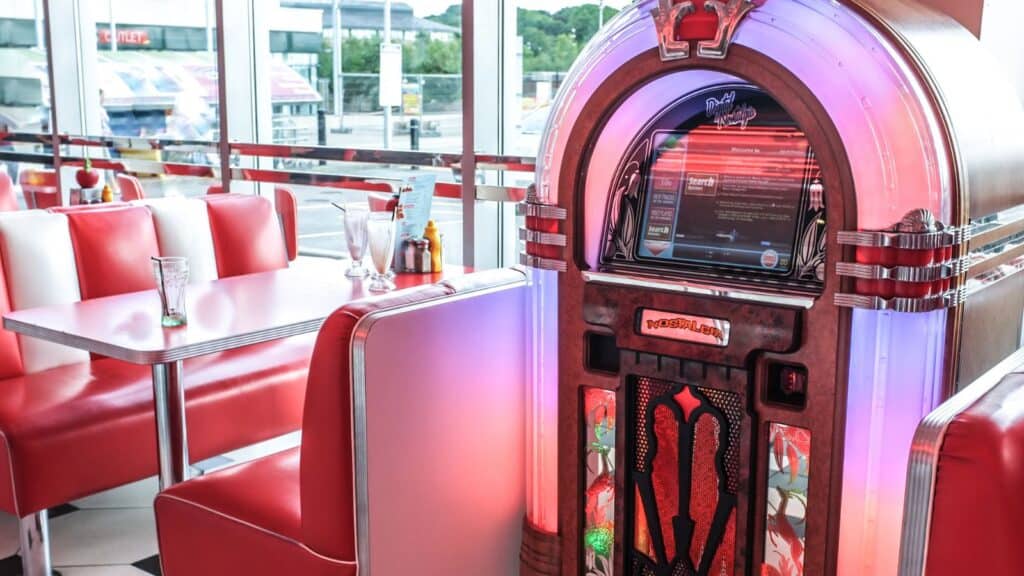 A retro jukebox stands beside red and white booth seating in a diner with large windows and outdoor views, evoking the classic charm that makes diner chains be everywhere across the country.