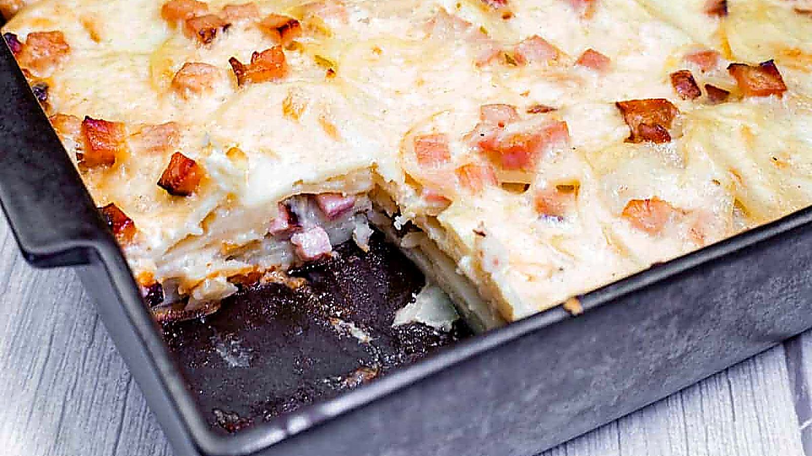 A rectangular pan of Scalloped Potatoes with Ham and Cheese, partially sliced, showing layers.