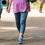 Three adults in athletic wear walk on a paved path outdoors, each carrying a rolled-up yoga mat. Only their legs and torsos are visible.