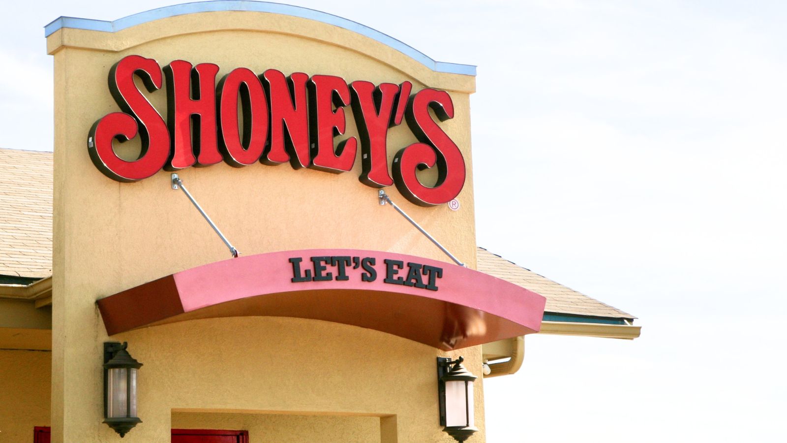 The exterior of a Shoney’s restaurant, one of America’s classic salad bar chains, features a bold red sign and the words “LET’S EAT” displayed above the entrance.