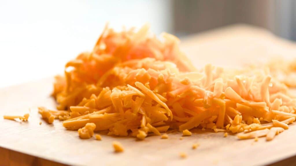 Shredded cheddar cheese from top store brands sits on a wooden cutting board, showcasing the quality that companies behind the label deliver.