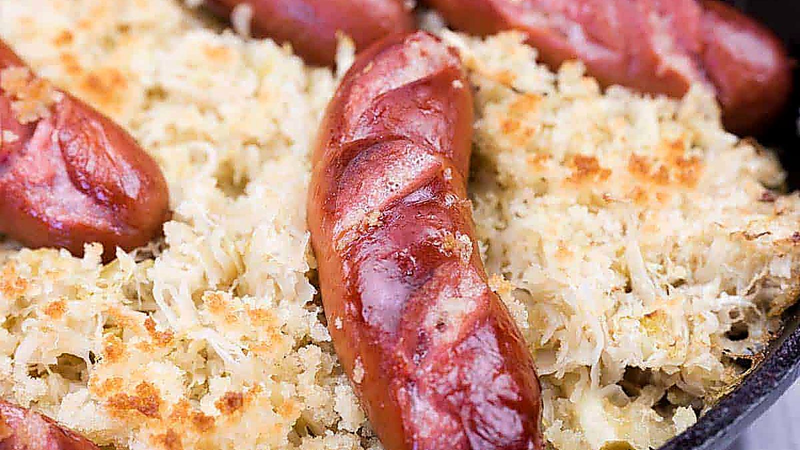 Close-up of browned sausages on a bed of sauerkraut and breadcrumbs in a baking dish.