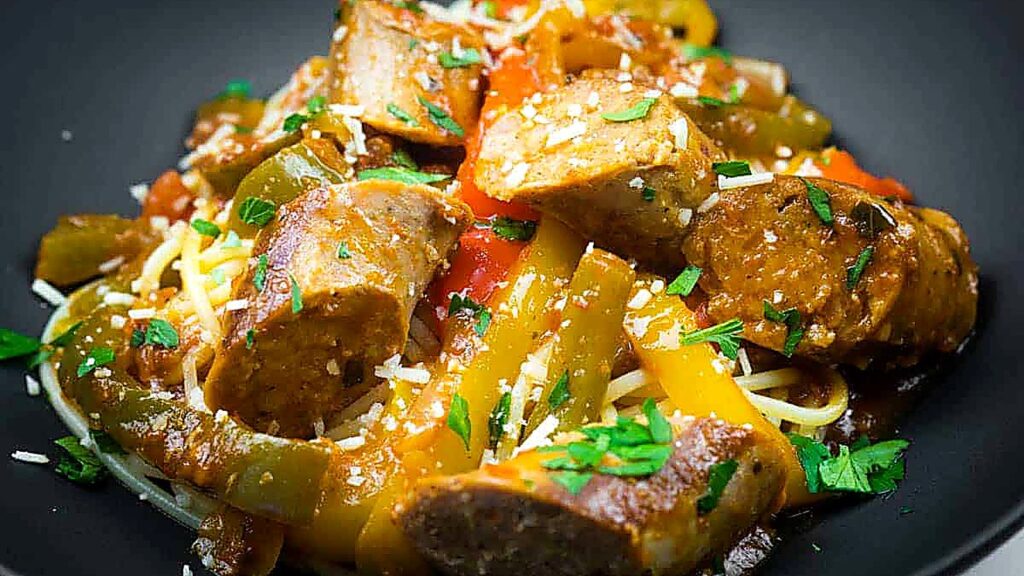 A plate of spaghetti topped with sliced sausage, bell peppers, tomato sauce, and garnished with chopped parsley and grated cheese.