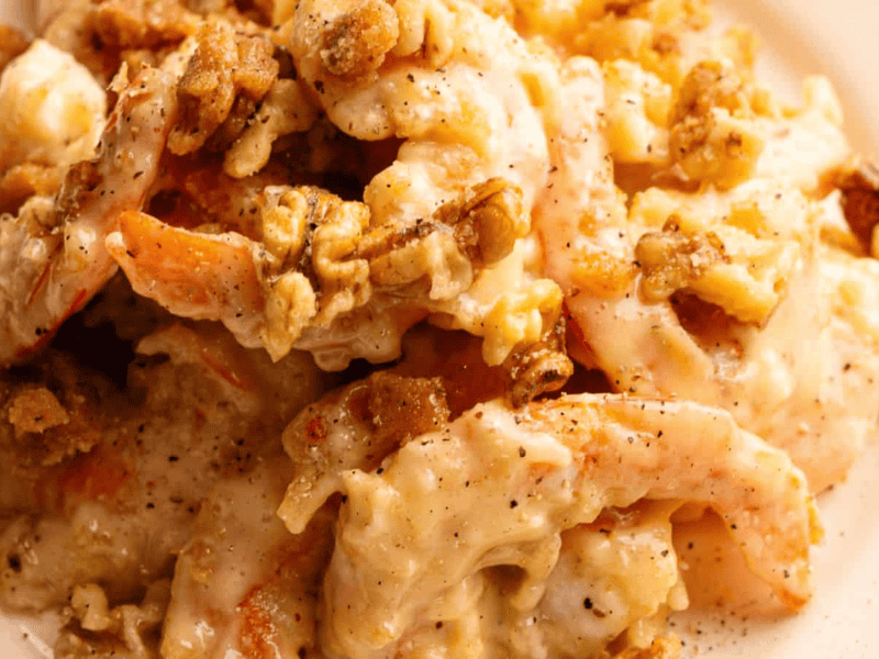 Shrimp coated in a creamy sauce, topped with chopped walnuts, served on a white plate.