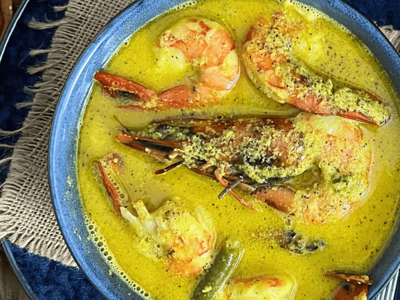 A bowl of Shrimp Coconut Curry Instant Pot, served on a blue woven placemat with a spoon on the side.