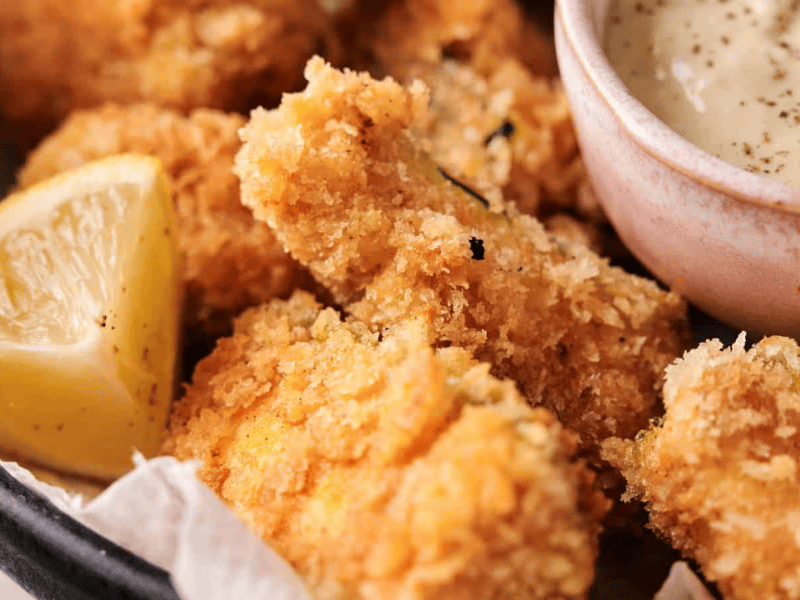 Close-up of breaded chicken nuggets with a lemon wedge and a small bowl of dipping sauce.