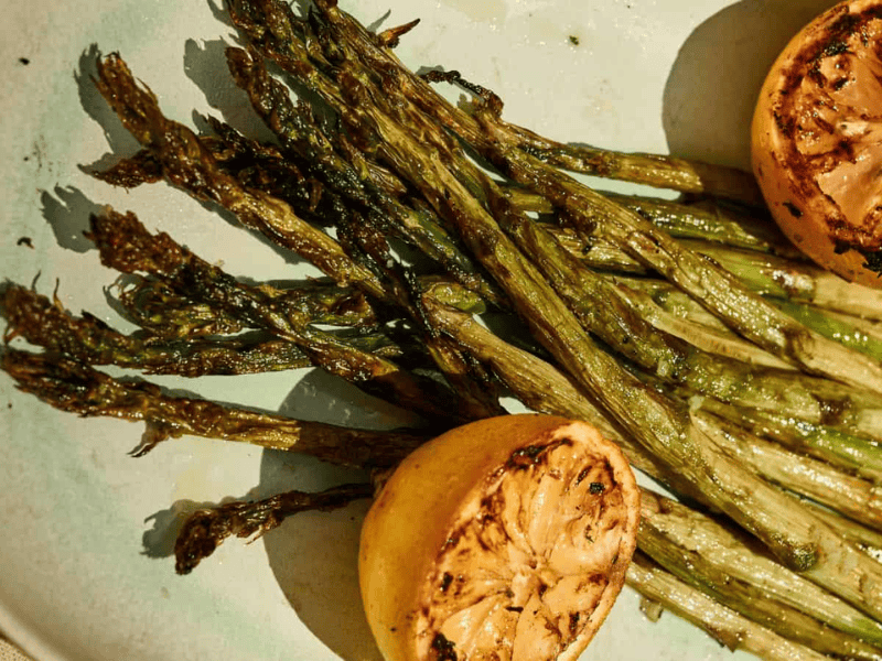 Grilled asparagus spears served on a plate with two charred lemon halves.