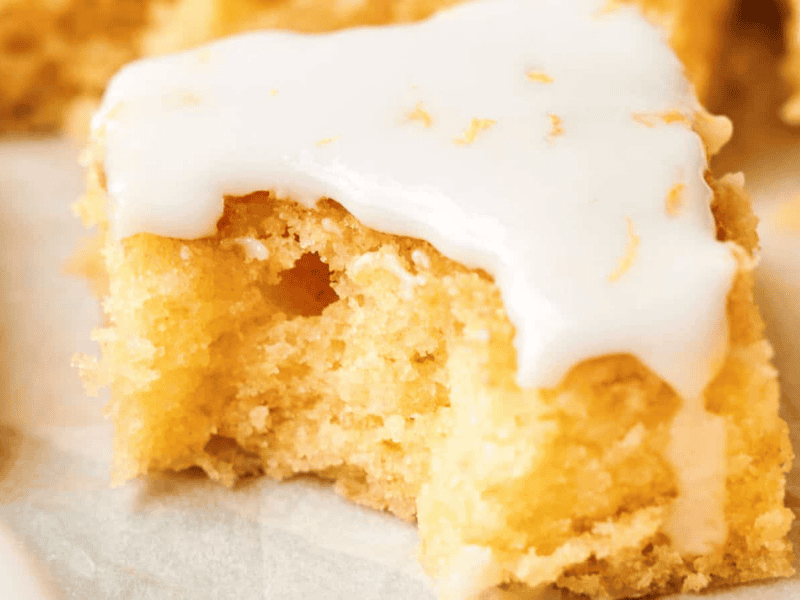 Close-up of a square piece of yellow cake with a smooth white icing layer on top, sitting on a light-colored surface.
