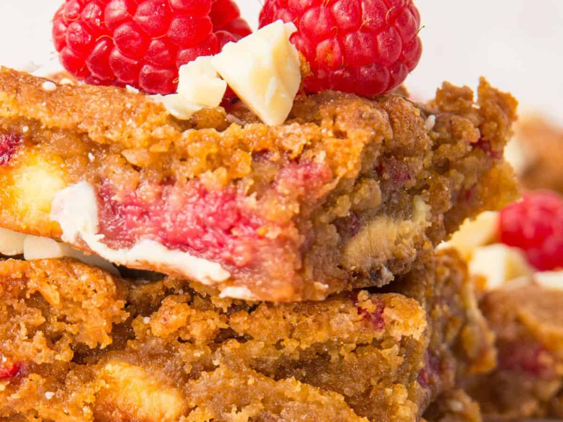 Close-up of Raspberry and White Chocolate Blondies filled with white chocolate chips and raspberries, topped with fresh raspberries and white chocolate chunks.