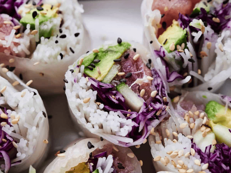 Close-up of sliced spring rolls filled with rice, avocado, purple cabbage, and sesame seeds, arranged on a white plate.