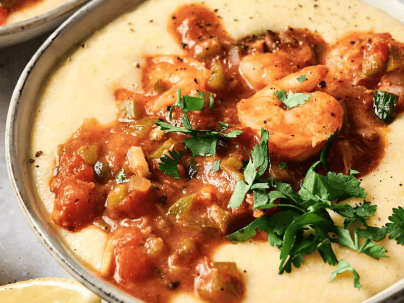 A bowl of creamy grits topped with shrimp in a tomato-based sauce and garnished with fresh parsley.