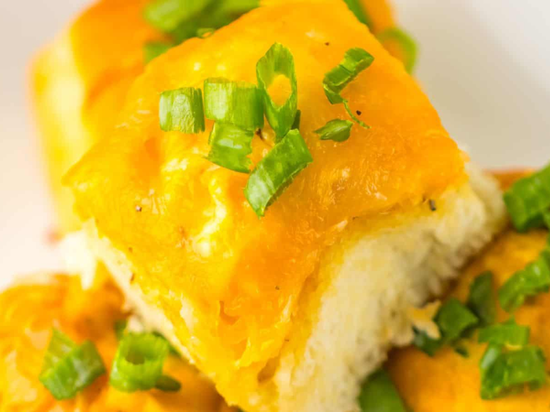 Close-up of cheesy garlic bread rolls topped with chopped green onions on a white plate, reminiscent of Loaded Buffalo Chicken Rolls.