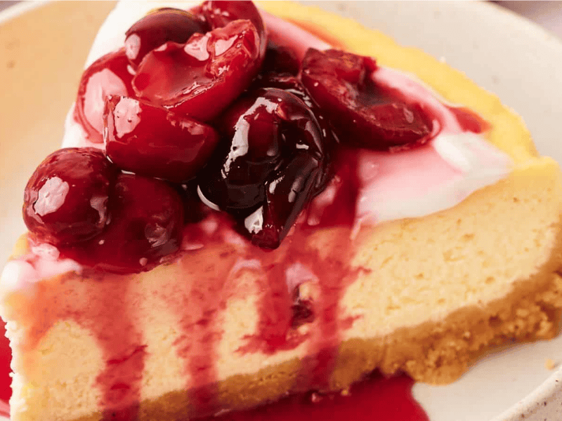 A slice of cheesecake topped with cherry sauce, sitting on a beige plate.
