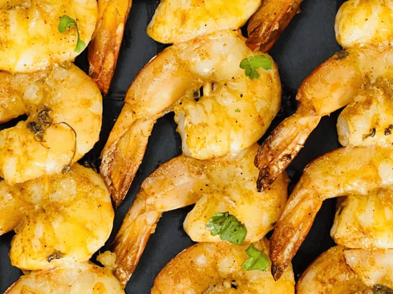 Grilled shrimp skewers seasoned with spices and garnished with fresh herbs, served on a dark plate.