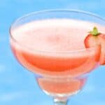 A pink frozen drink served in a glass with a sliced strawberry garnish, set against a blue background.