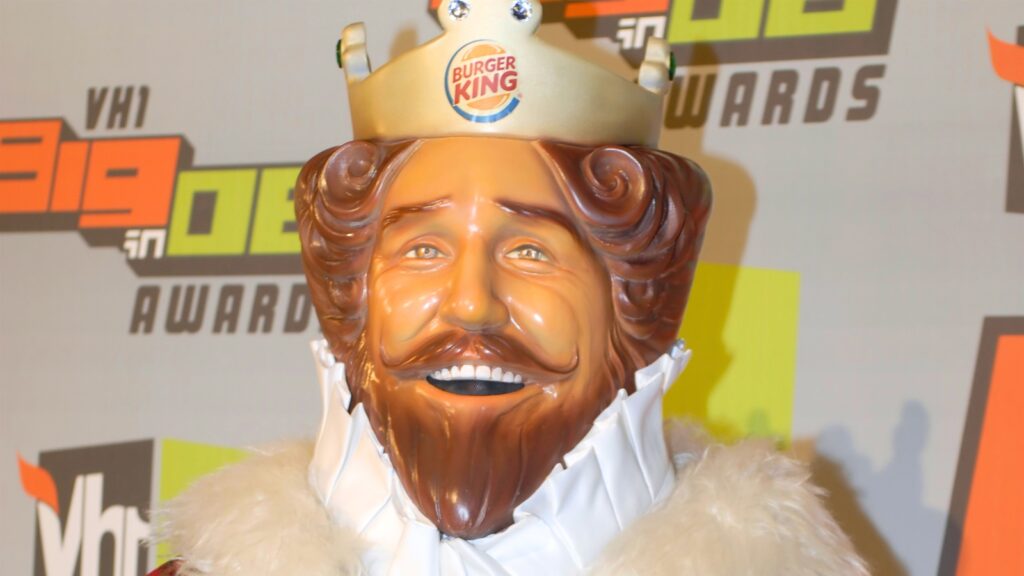 A person dressed as one of the iconic brand mascots, the Burger King, complete with a crown, stands in front of a VH1 awards event backdrop.