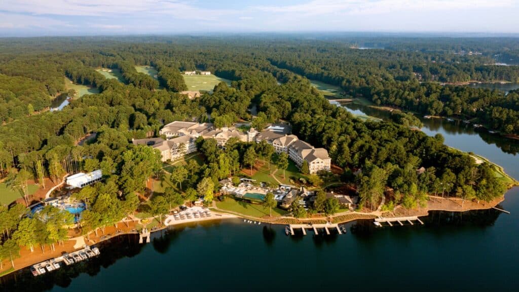 Aerial view of a large lakeside resort surrounded by dense forest, with docks, pools, and buildings near the shoreline.