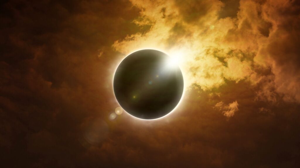 A solar eclipse with the sun partially visible behind the darkened moon, surrounded by glowing clouds in the sky.