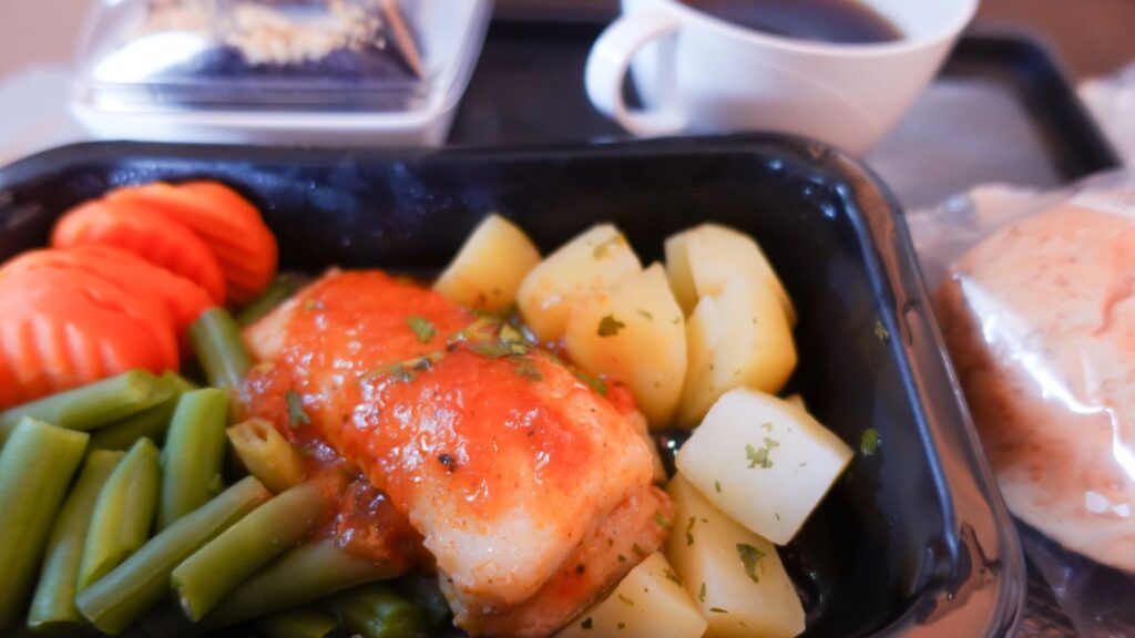 Tray with chicken in sauce, diced potatoes, green beans, sliced carrots, a bread roll, a slice of cake in a container, and a cup of coffee—this classic frozen dinner shaped the American freezer for generations.
