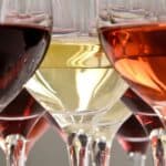 Close-up of multiple wine glasses filled with red, white, and rosé wine, showing the different colors and reflections in the glass.