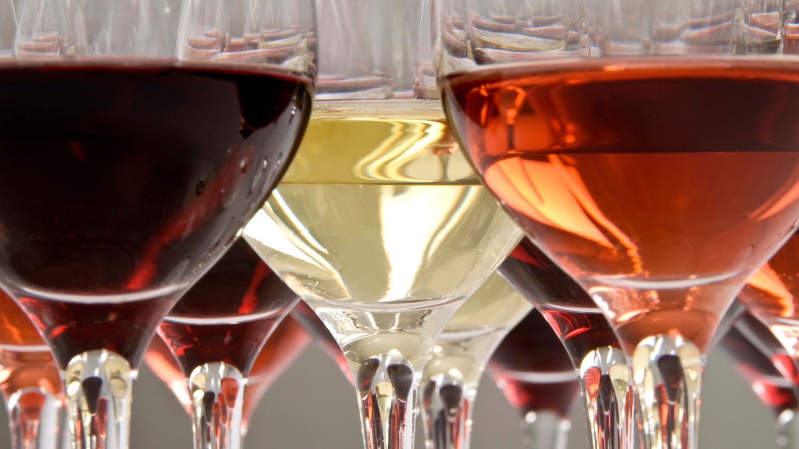Close-up of multiple wine glasses filled with red, white, and rosé wine, showing the different colors and reflections in the glass.