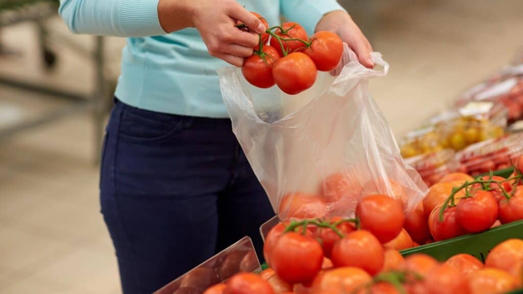 A person places red tomatoes&mdash;one of the grocery items whose prices rose&mdash;into a clear plastic bag at a grocery store produce section.
