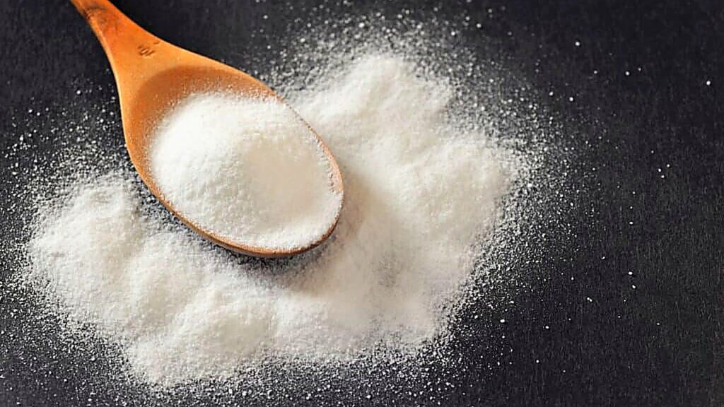 A wooden spoon rests on a pile of white, granular powder scattered on a dark surface.