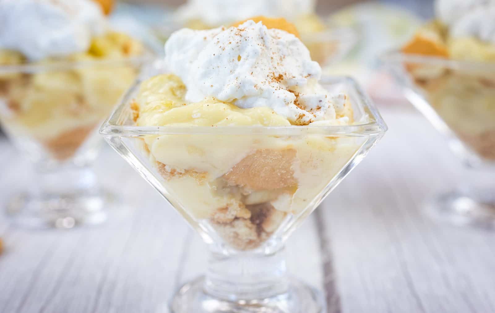 A glass dish filled with banana pudding, layered with cookies and topped with whipped cream and a sprinkle of cinnamon.