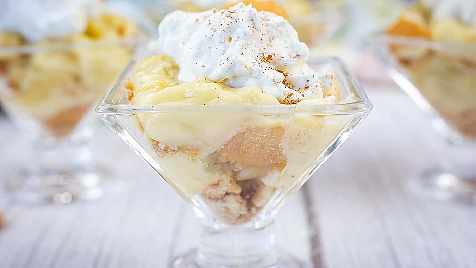 A glass dish filled with banana pudding, layered with cookies and topped with whipped cream and a sprinkle of cinnamon.