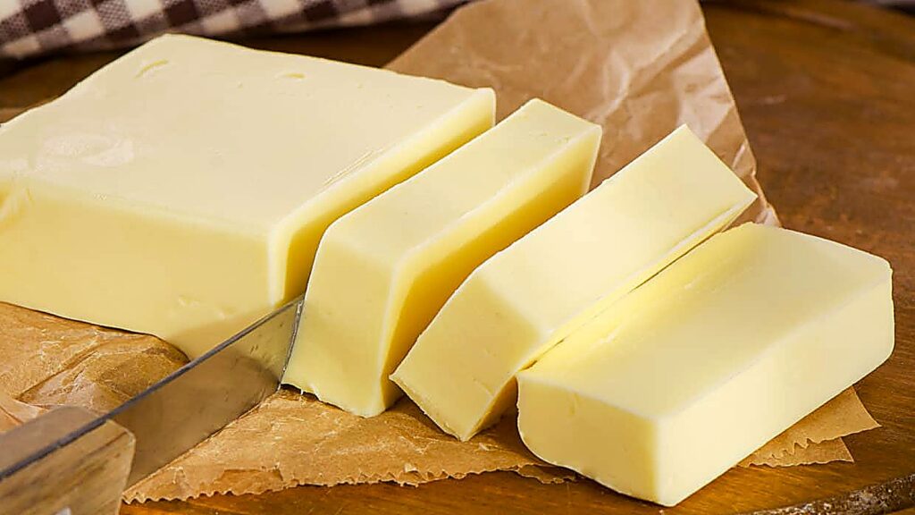 A block of butter being sliced with a knife on brown parchment paper.