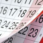 Close-up of overlapping pages from a paper calendar showing dates, with a page being flipped to reveal the next month’s dates underneath.