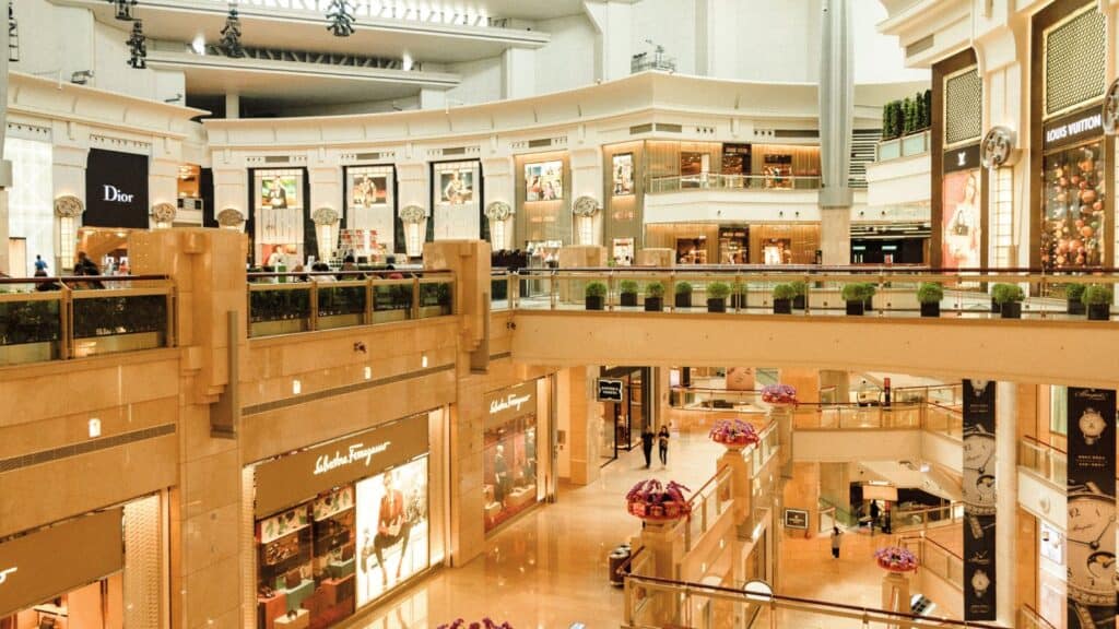 Interior view of a luxury shopping mall with multiple levels, high-end brand stores like Dior and Salvatore Ferragamo, and a few people walking and shopping.