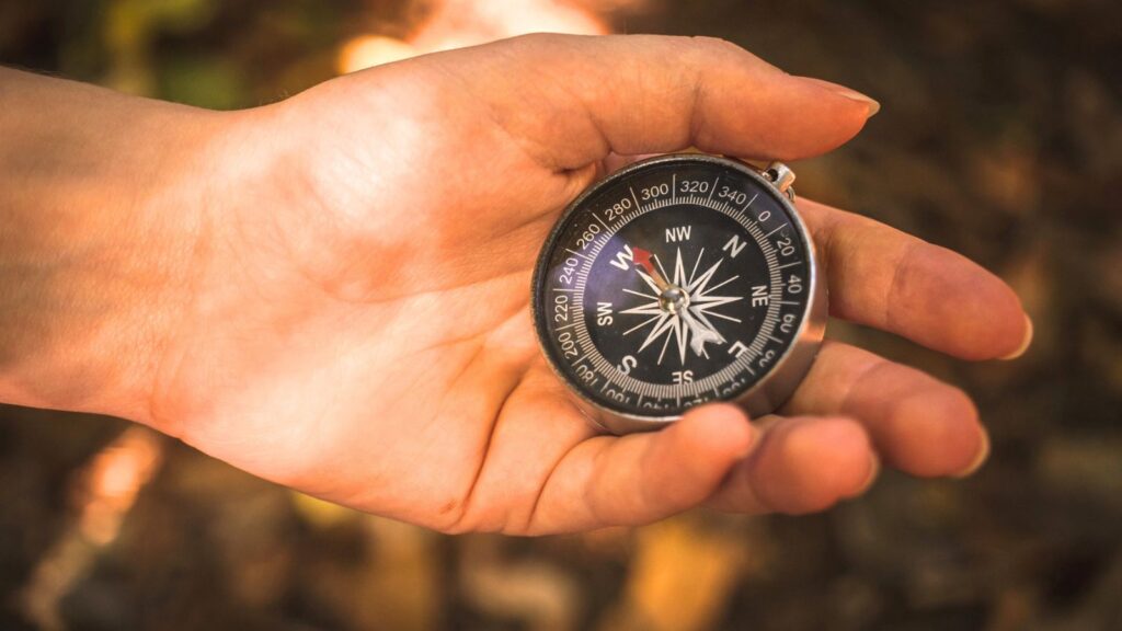 A person holds a black compass in their left hand, preparing for the Grand Forks treasure hunt, with a blurred natural background.