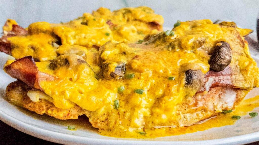 Two pieces of chicken topped with melted cheese, mushrooms, and sauce served on a white plate.