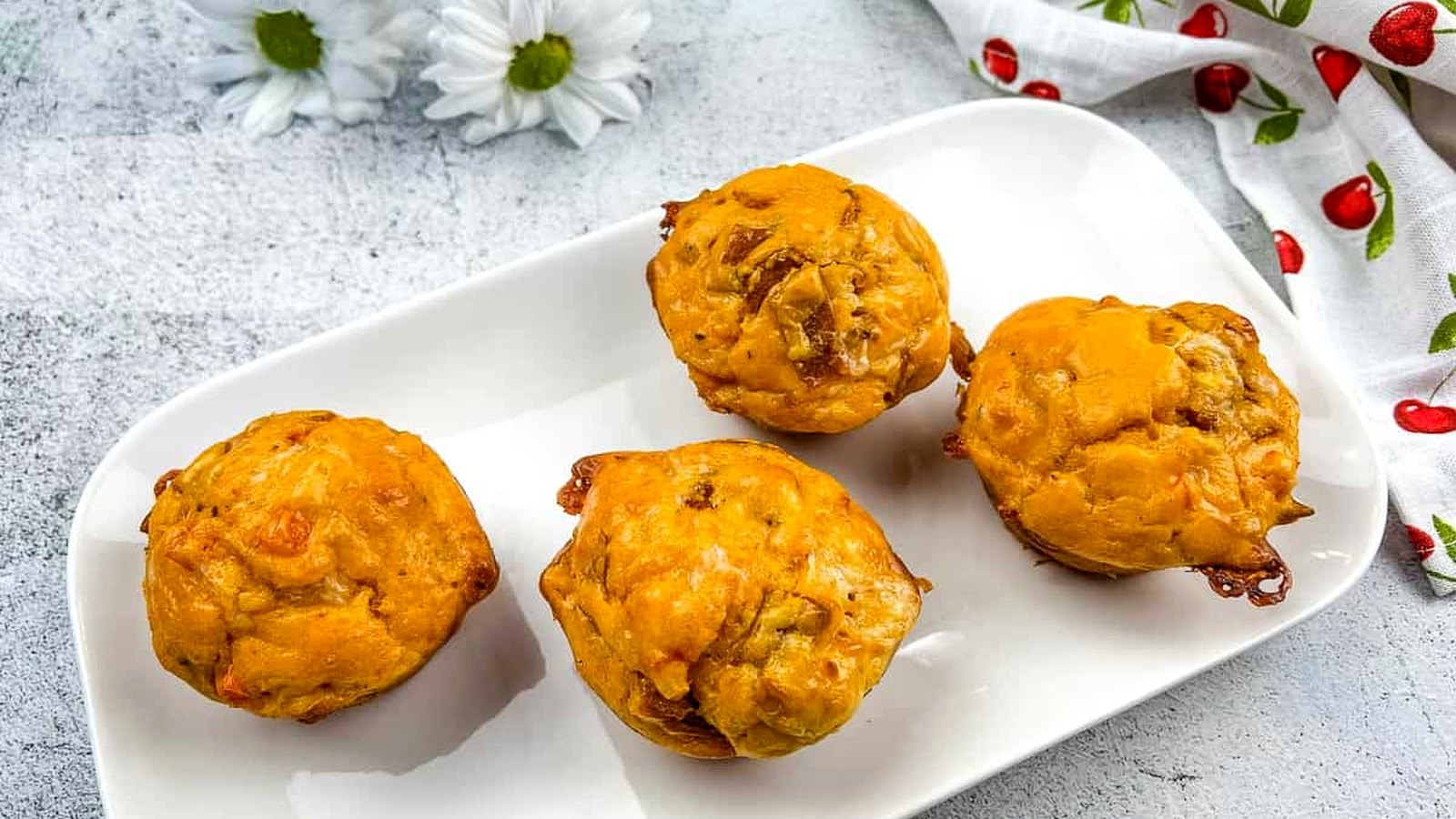 Four pizza muffins on a white plate with flowers.