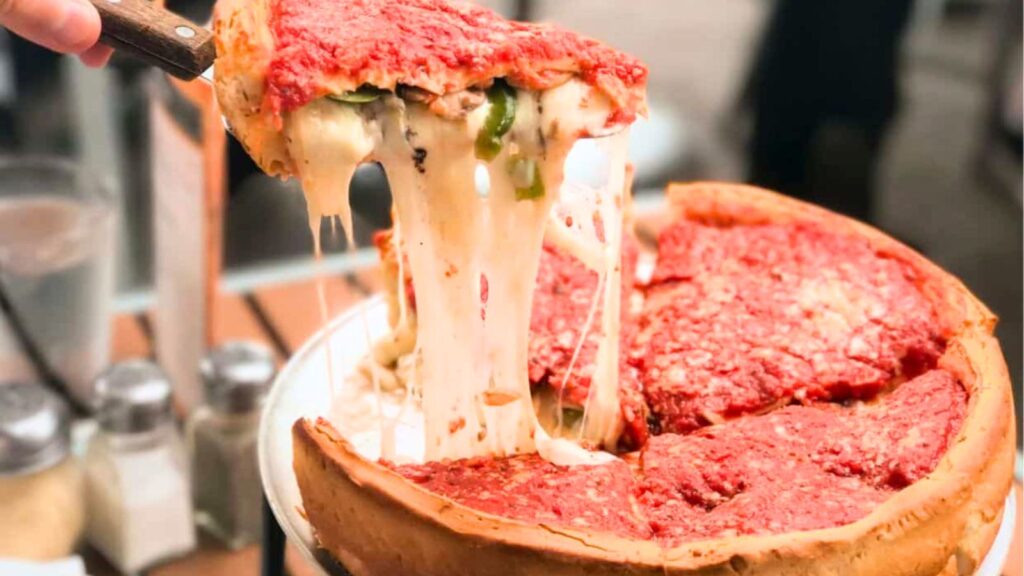 A slice of Chicago-style deep dish pizza with melted cheese being lifted from a pan, exposing the filling and thick crust&mdash;an irresistible sight that&rsquo;s even better when enjoyed with your Uno Pizza Pass.