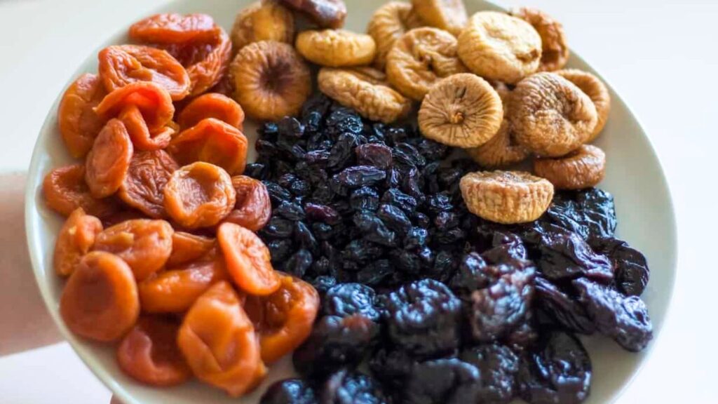 A plate with sections of dried apricots, dried figs, raisins, and dried prunes&mdash;healthy foods high in sugar&mdash;arranged in groups.