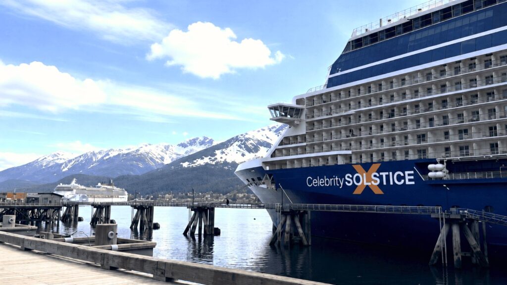 Two large cruise ships docked at a pier with snow-capped mountains and a partly cloudy sky in the background, reflecting the growing world cruise demand for breathtaking destinations and unforgettable travel experiences.
